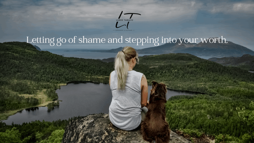 "Woman with blonde hair in a ponytail sitting on a cliffside with a brown dog, overlooking a lush green forest and lakes, with mountains and cloudy sky in the background. Text reads: 'Letting go of shame and stepping into your worth' with the name and logo 'Loree Tamayo – Speaker & Author' above."
